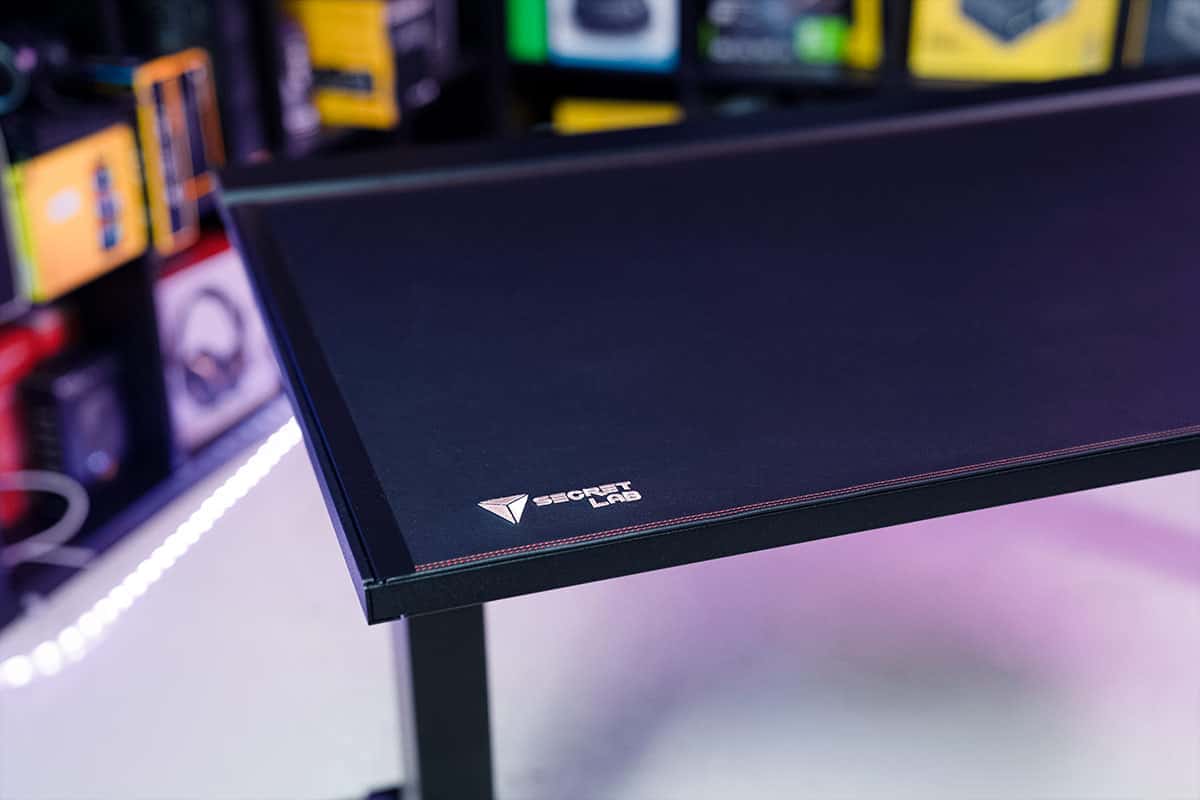 A black gaming table in a room full of electronics is featured in the Secretlab Magnus Pro review.
