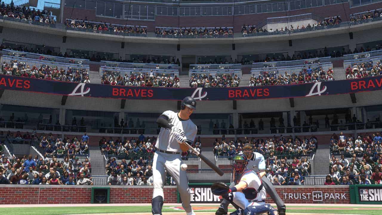 A baseball batter prepares to swing at a pitch during a game at an MLB The Show 24 stadium with spectators in the stands.