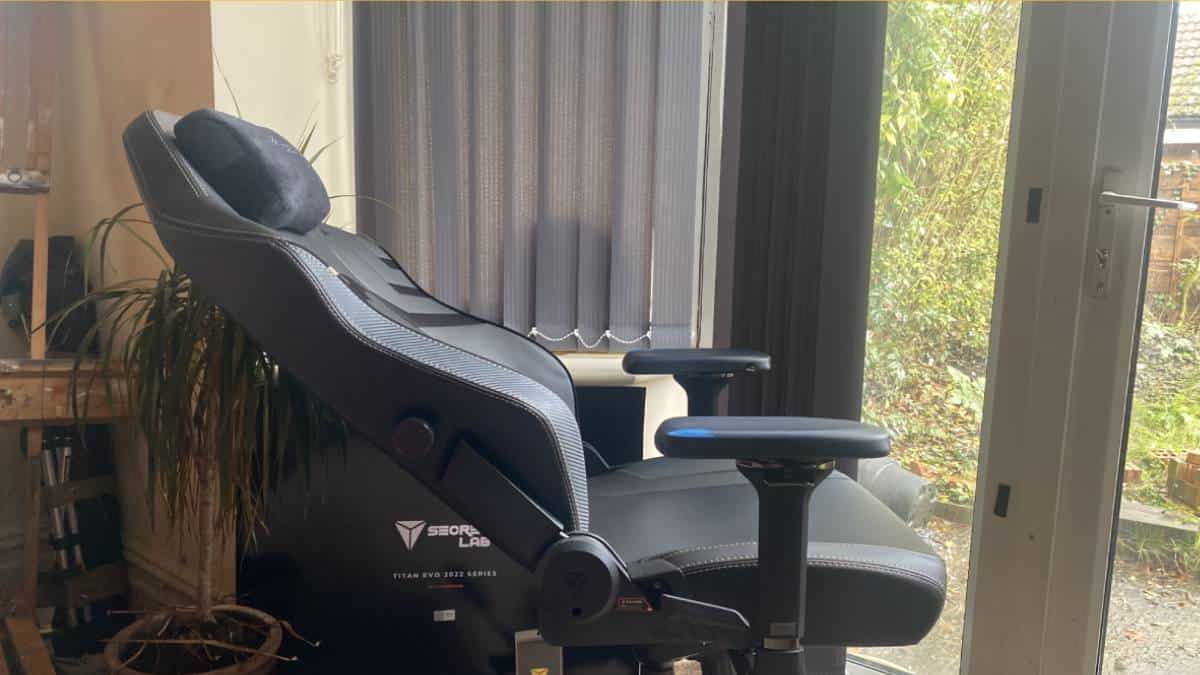 The SecretLab Titan EVO, a black gaming chair, is elegantly placed in front of a window, reclining fully.